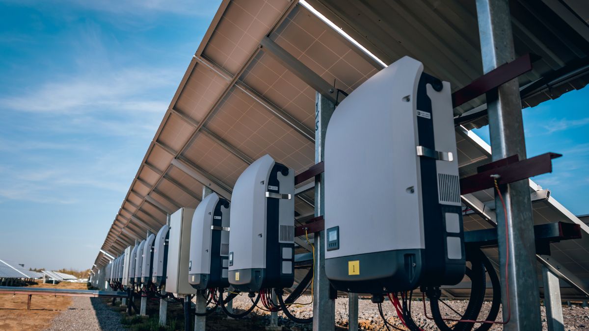 Napelemek és inverterek sorakoznak egy napenergia-telepen, világos égen.